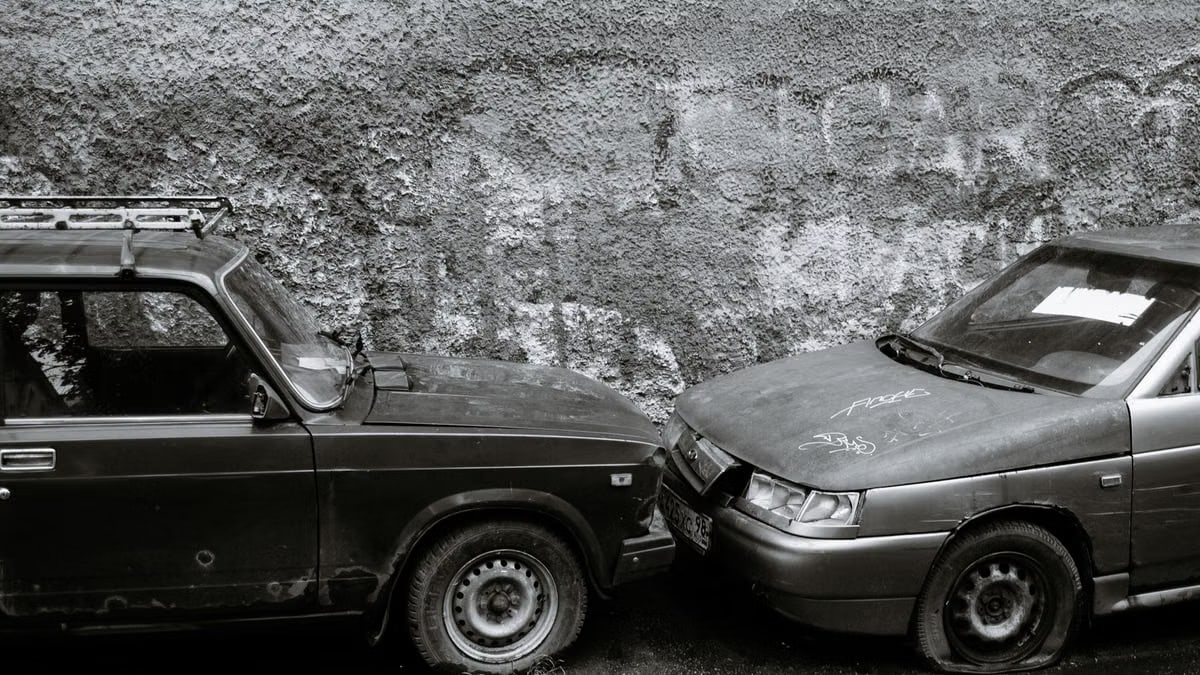 Black and white of aged automobiles with deflated tires near gray wall on street